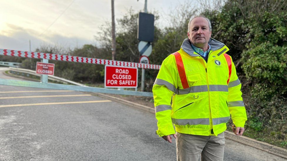 Mike Rigby in a hi-vis jacket stands in front of a road closure