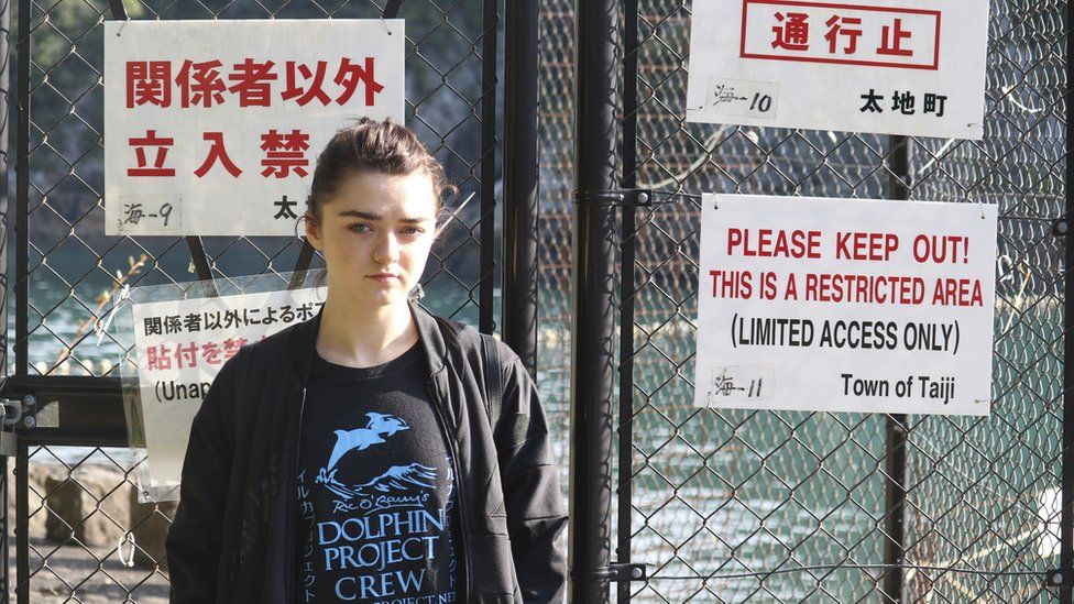 British actress Maisie Williams stands in front of a fence with notice boards beside the beach known for dolphin hunting in Taiji, central Japan