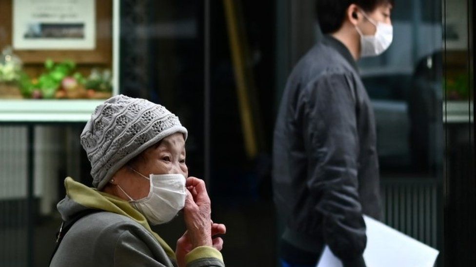 A woman wearing a face mask, amid concerns of the COVID-19 coronavirus, touches her face on a street in Tokyo on April 6, 2020.
