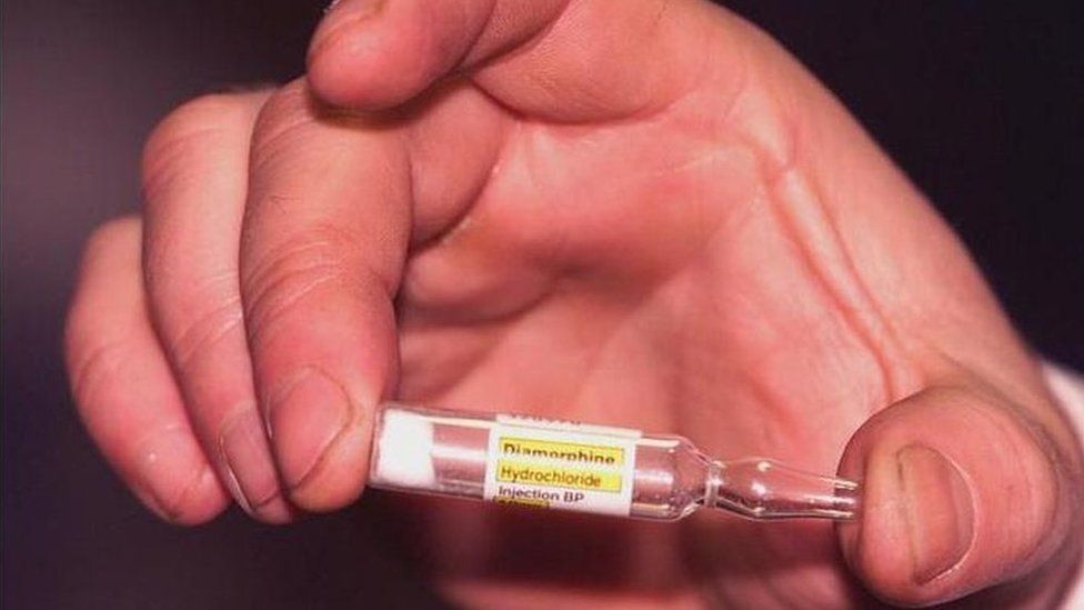 A hand is seen holding a phial of diamorphine hydrochloride, the medical name for heroin
