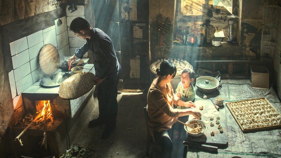 Family preparing food indoors, with rays of sunlight shining through the windows