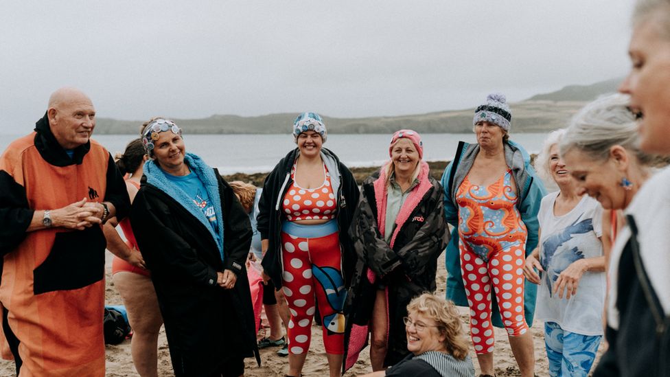 A group of people stood on a beach in swimming wear laughing