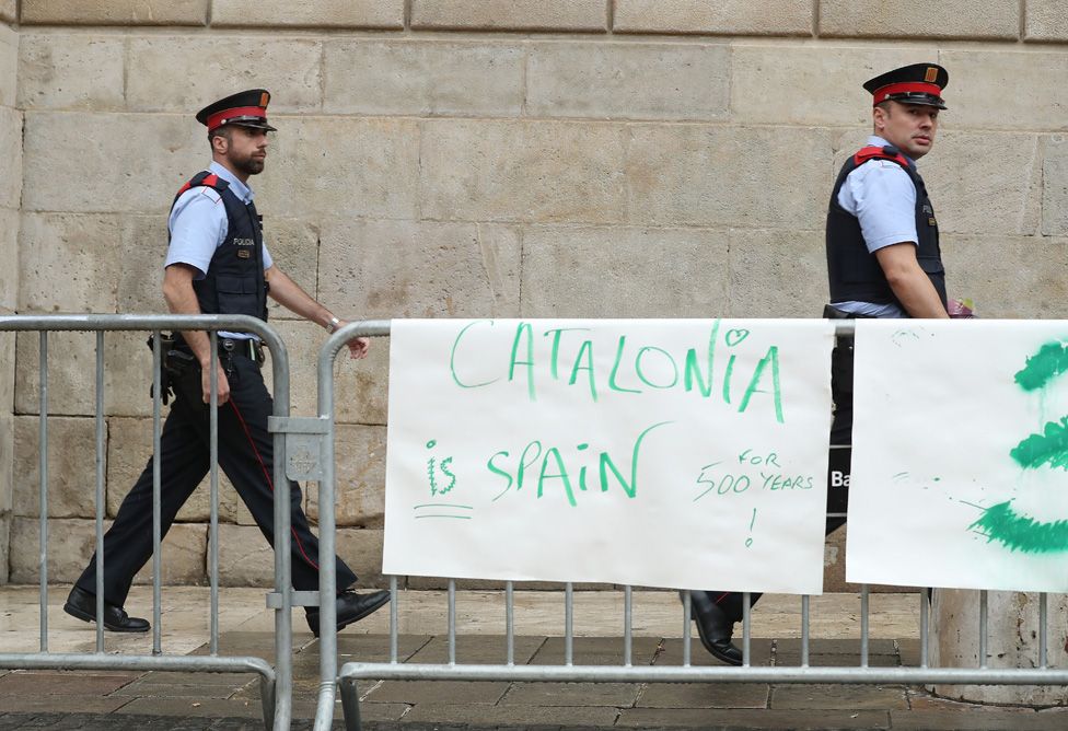 Catalan police officers walk past a "Catalonia is Spain" poster