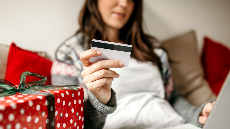 A woman spending money online next to Christmas presents