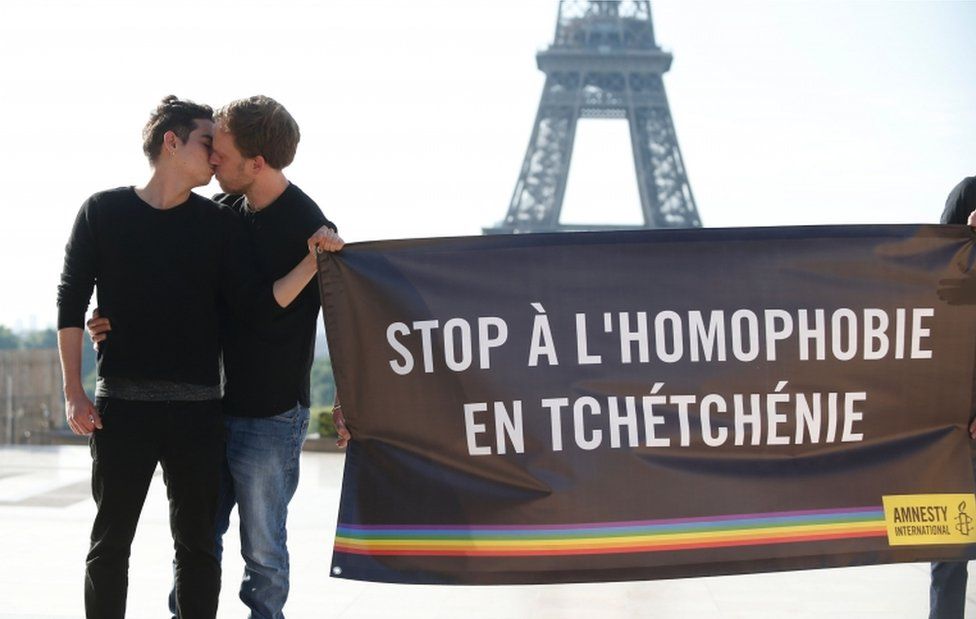 Amnesty International activists kiss each others as they hold a banner, reading "Stop homophobia in Chechnya", to denounce persecution against LGBT community in Chechnya on 29 May 2017 in front of the Eiffel tower in Paris