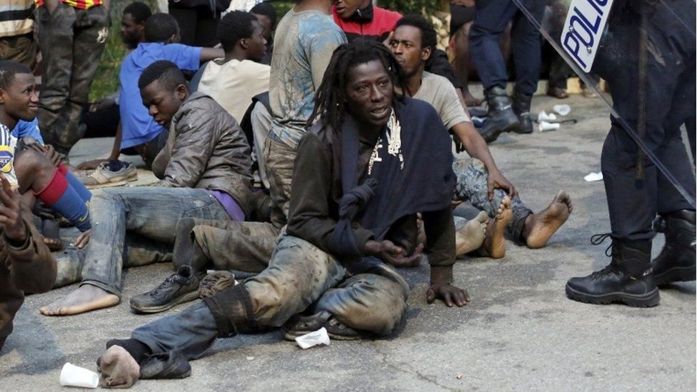 Migrants sit on the ground next to Spanish police officers after storming a fence to enter the Spanish enclave of Ceuta on 17 February 2017