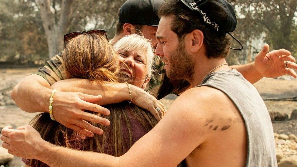 Family hugging amid burnt ruins of their home