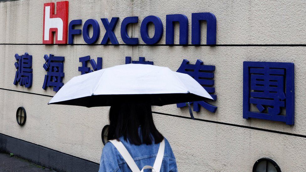 Женщина с зонтиком проходит мимо логотипа Foxconn возле здания компании.