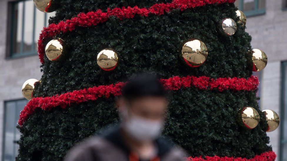 A masked man walks past a Christmas tree