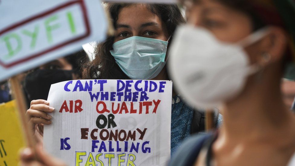 A protester holding a sign that says: "Can't decide whether air quality or economy is falling faster"