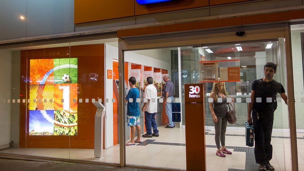 Customers and visitors using the cash machine ATM dispensers inside the secure lobby of Itau, one of Brazil's major banks