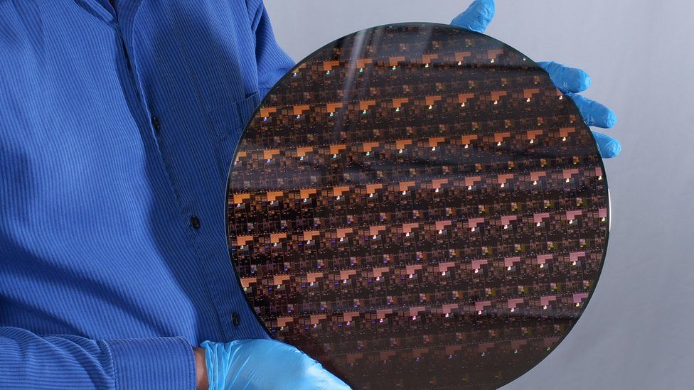 A person wearing gloves holds a circular sheet with a repeating pattern of silicon chips