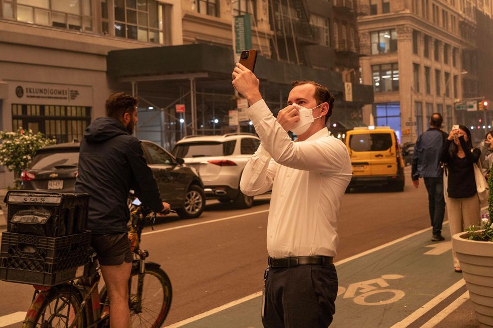 A man wearing a face mask takes a photo of hazy New York, US, because of bad air quality brought in by smoke of Canadian wildfires on 7 June 2023