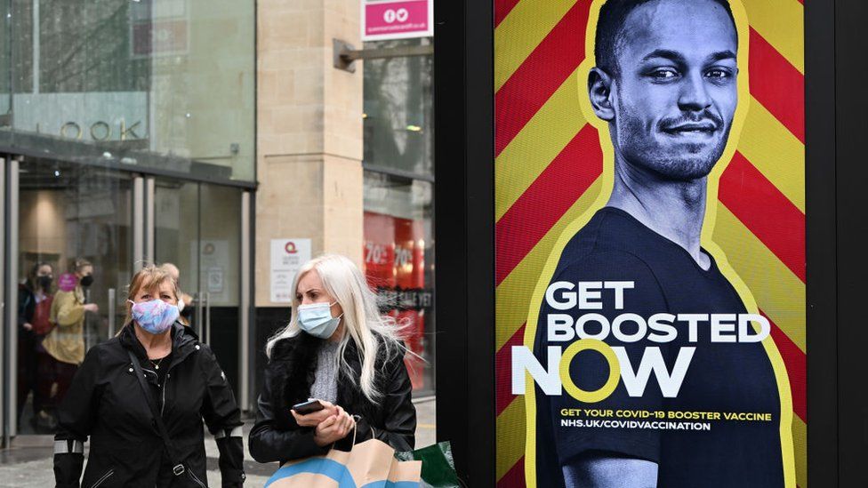 Two women next to a sign saying Get Boosted Now