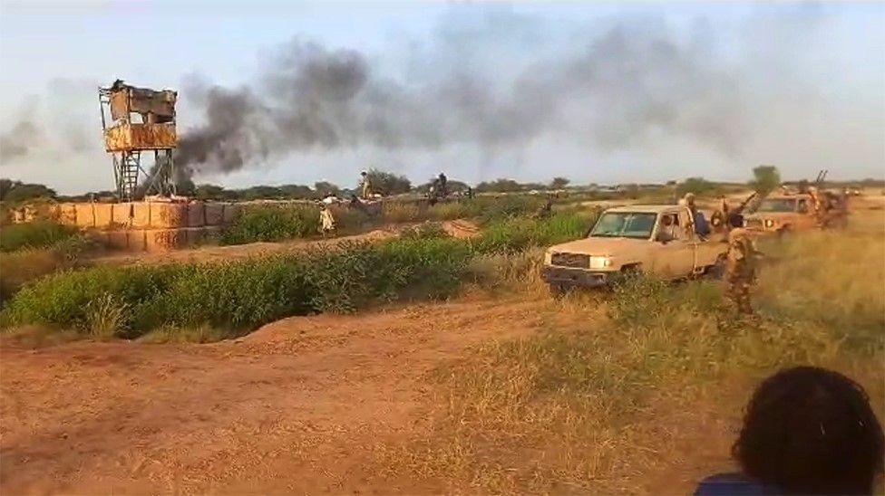 A watchtower and a burning military base behind a group of rebel fighters