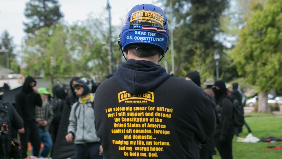 A man in an Oath Keeper hoodie and a helmet