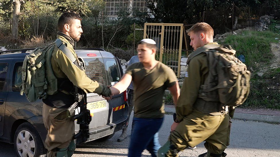 An Israeli soldier (L) shakes hands with an Israeli settler (R) who attacked Yasser Abu Markhiya in Hebron, in the occupied West Bank