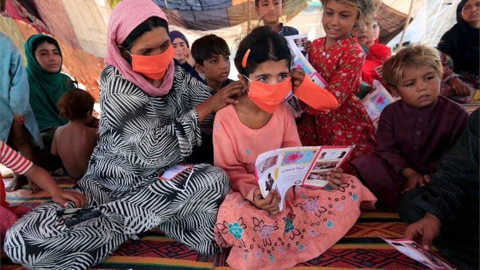 An internally displaced woman helps a girl put on a face mask distributed by Unicef