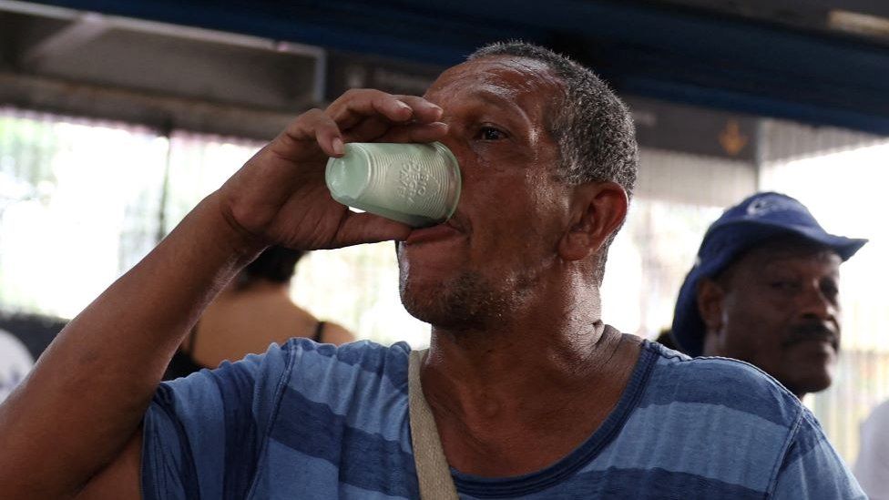 Man drinking glass of cold water in heat wave at train station in Rio de Janeiro