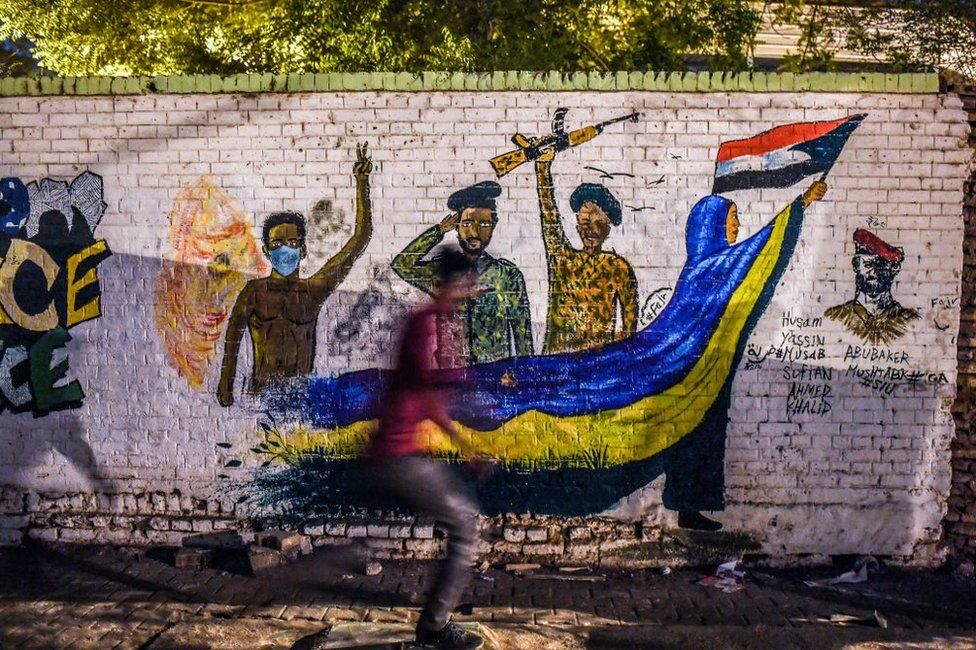 A Sudanese protester runs past mural depicting scenes from recent demonstrations.