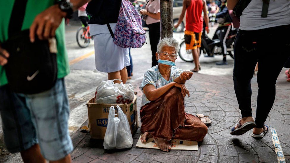 Пожилая женщина в медицинской маске просит милостыню в Маниле.