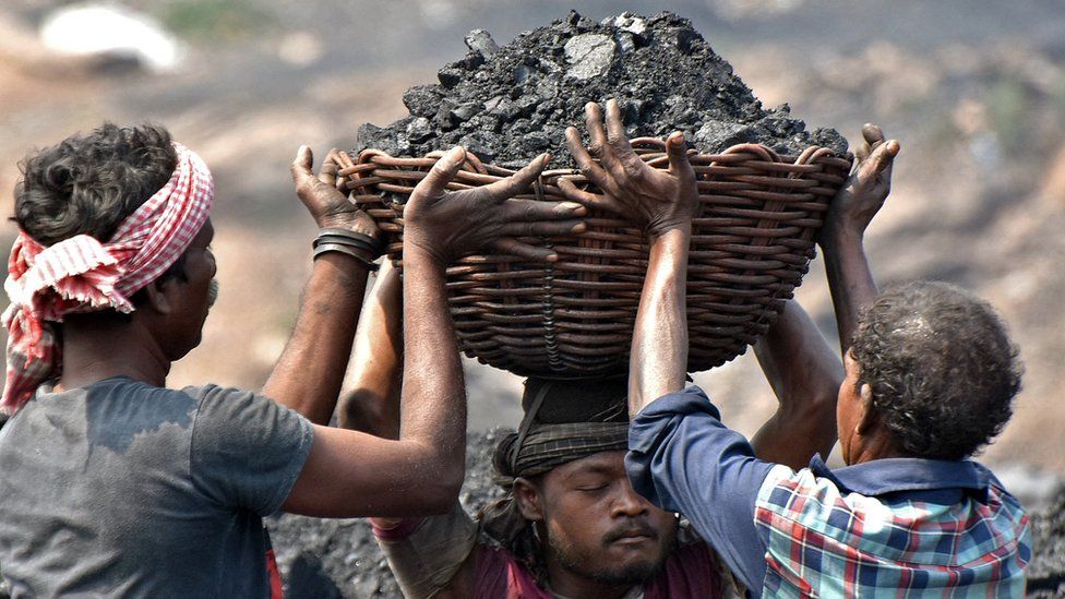 Two workers help a colleague load a basket of coal on his head to be carried in a loading truck