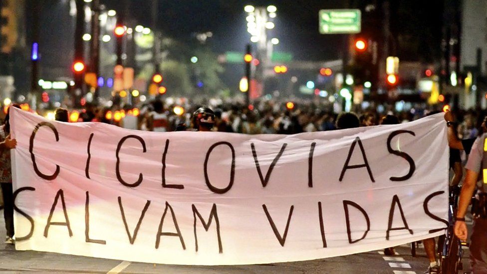 A banner reading "Bike lanes save lives" is held up during a protest by cyclists