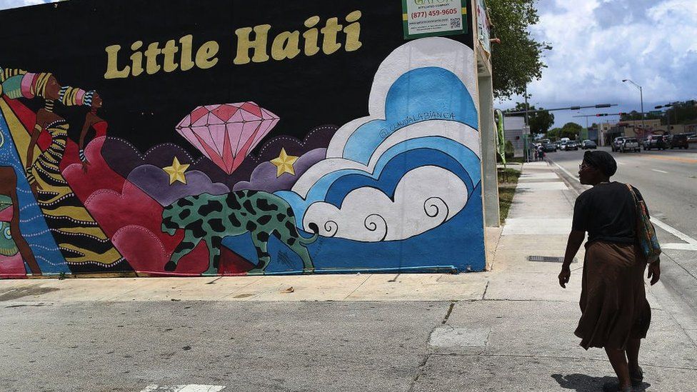 Woman walking past mural of showing a sign of Little Haiti