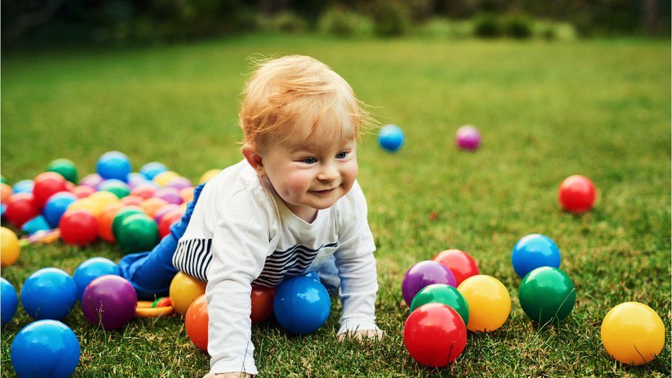 Baby crawling through colourful balls in a garden