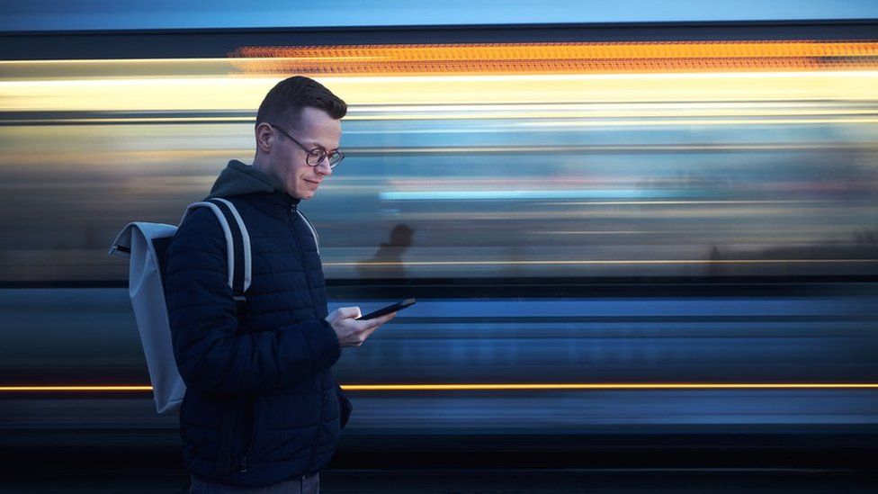 Man with backpack holding and using phone against train in blurred motion - stock photo