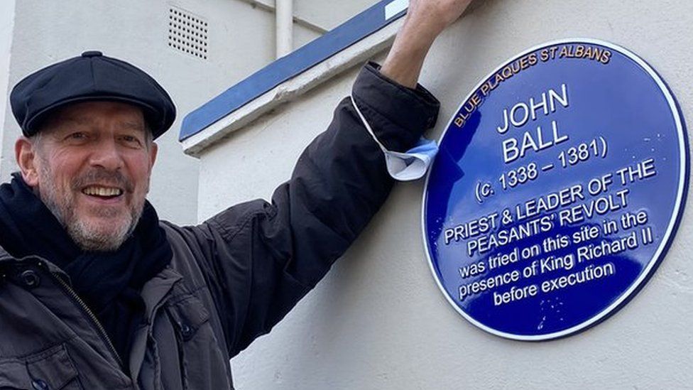 Tim Boatswain standing next to a blue plaque that has been unveiled to John Ball the leader of the Peasants' Revolt in 1381