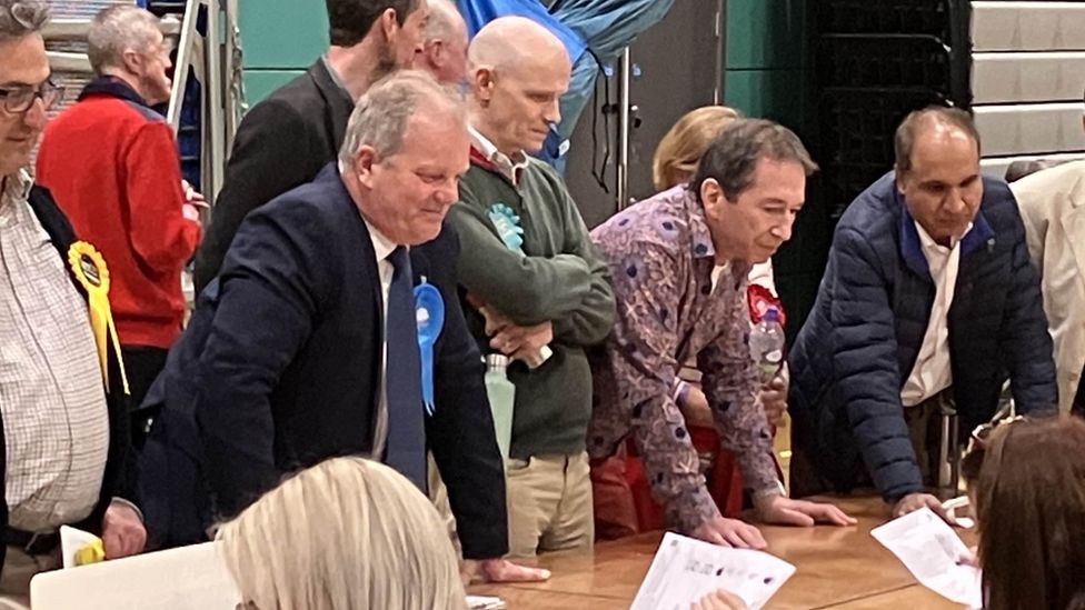 Andrew Williams, wearing a blue rosette, checking ballot papers as they are counted.