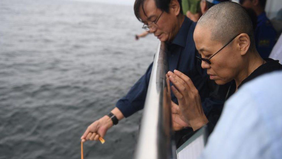 Liu Xiaobo's wife Liu Xia (R) prays as his ashes are scattered in the sea near Dalian