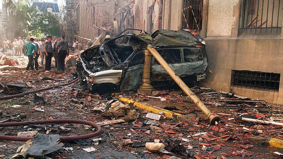 Police and rescue workers stand near destroyed cars and debris on March 17, 1992 in Buenos Aires shortly after a powerful bomb ripped through the Israeli Embassy