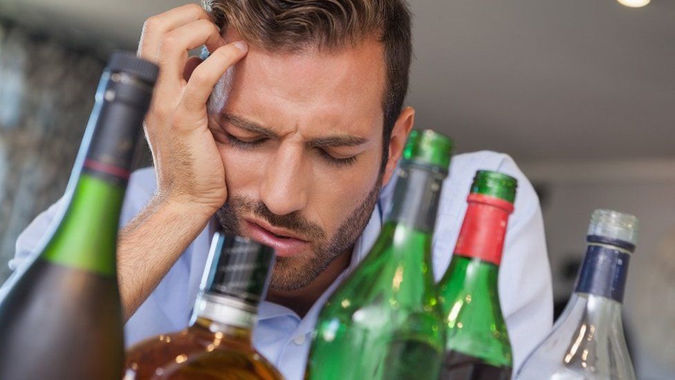 Man with hangover in front of empty bottles
