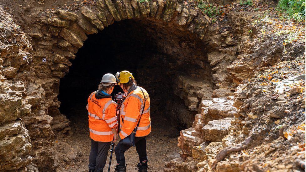 Two men in orange hi-vis jackets and hard hats standing in the entrance way of the Grotto tunnel