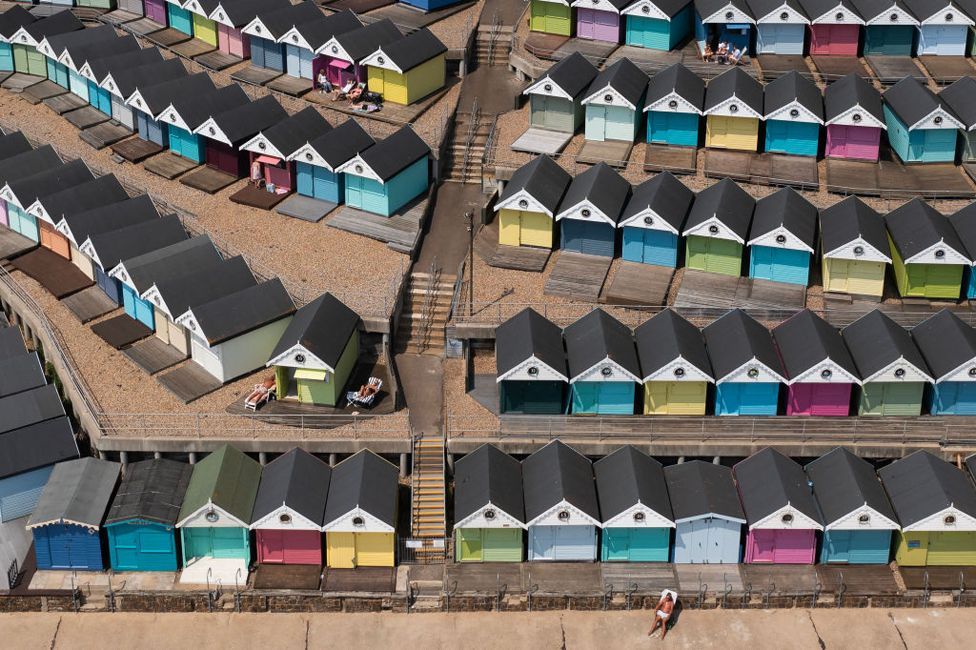 Aerial photo showing a man sunbathing in front of a row of beach huts on June 26, 2024 in Walton-On-The-Naze, England