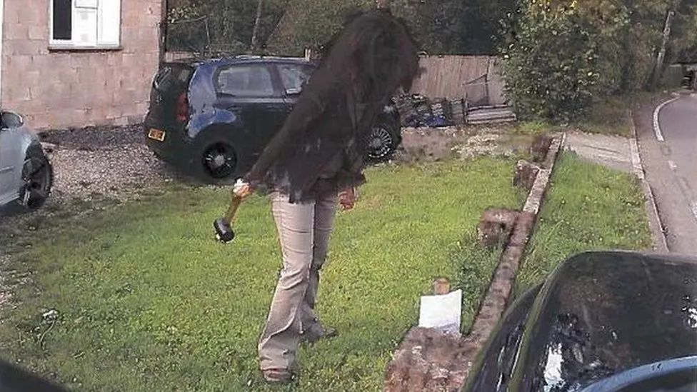 A West Berkshire Council officer standing in Maria Dobson's garden, with a mallet in her hand, standing next to a notice she hammered a post with the notice into her garden