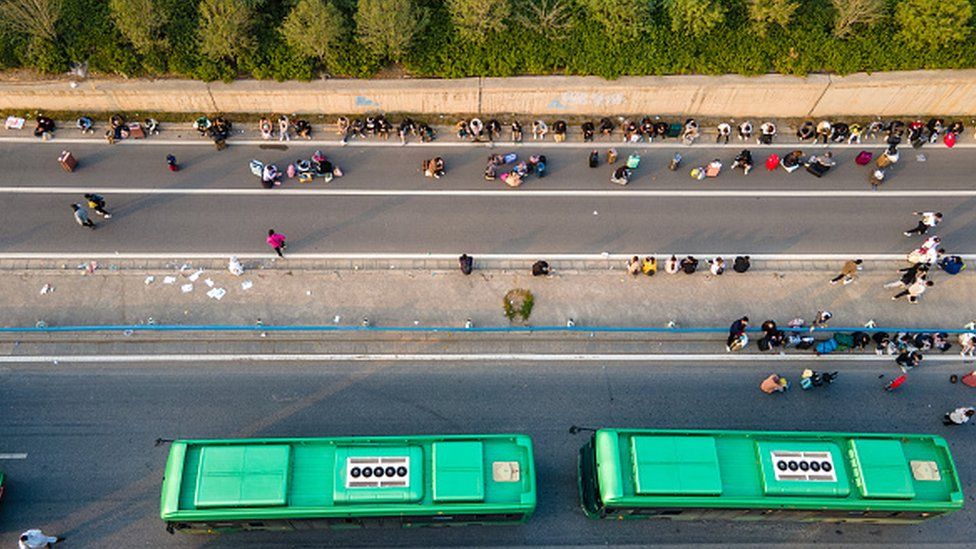 Foxconn workers resting on one side of a highway and two buses parked on the other side