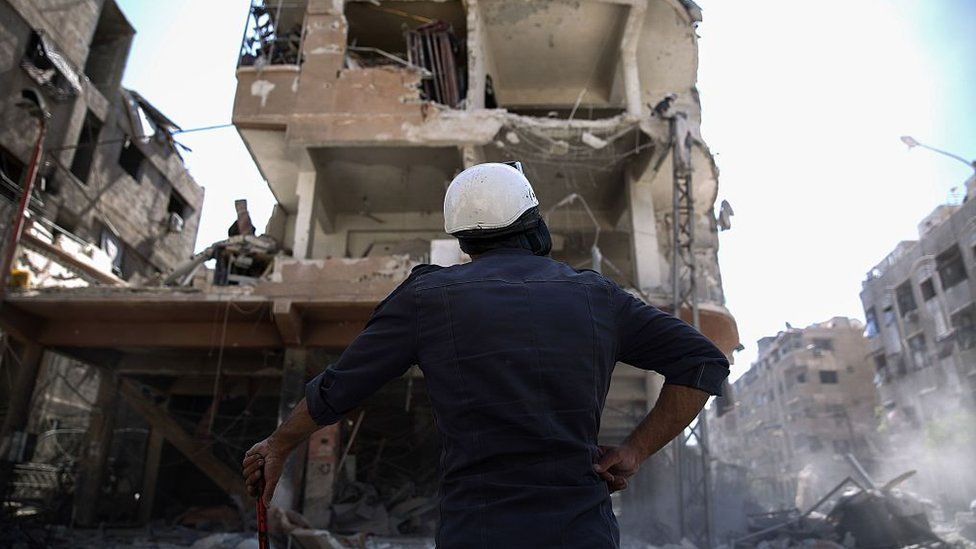 A member of the Syrian civil defence volunteers, known as the White Helmets, looks at a destroyed building following a reported air strike on the rebel-held town of Douma, on the eastern outskirts of the capital Damascus