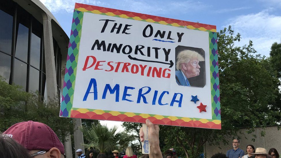 A demonstrator in Texas holds aloft a sign with a caricature of Donald Trump and the words: The only minority destroying America