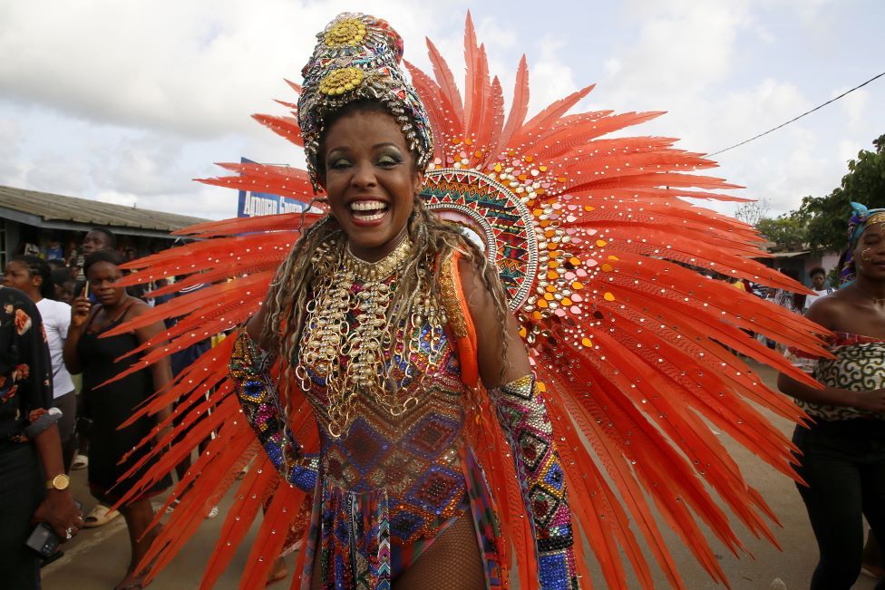 A woman from a troupe from Trinidad and Tobago smiles and dances in a bright orange outfit.