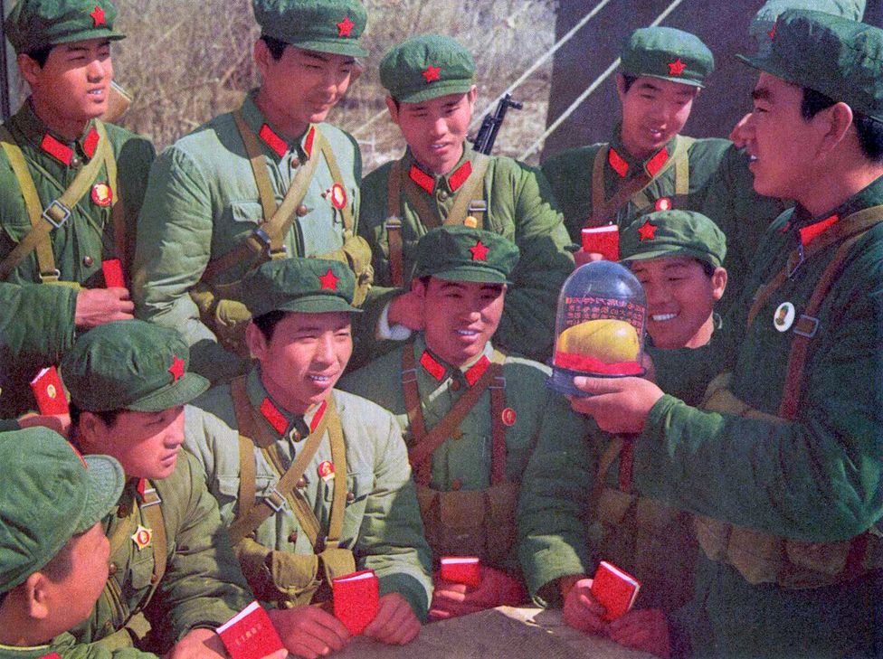 Members of the People's Liberation Army look at a wax replica mango in a glass case