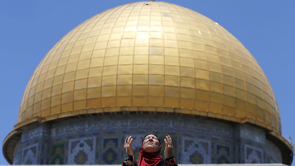 A Palestinian woman prays in front of the Dome of the Rock