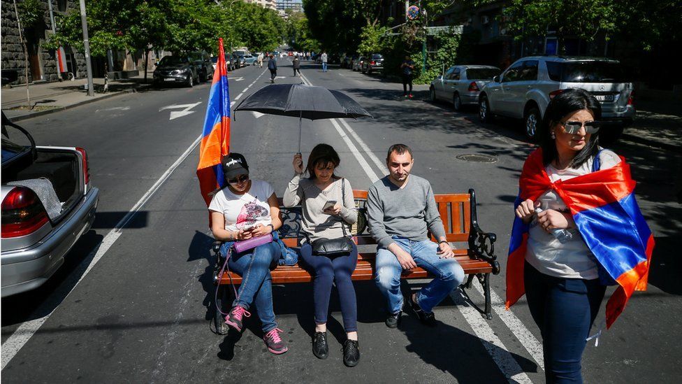 Armenian opposition supporters sit on bench as they block a road