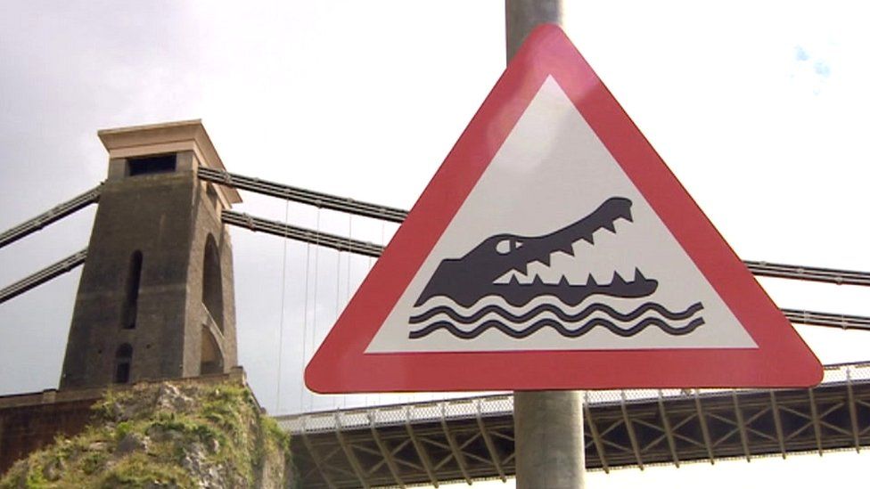 A crocodile warning red triangle sign, with the Clifton Suspension Bridge in the background