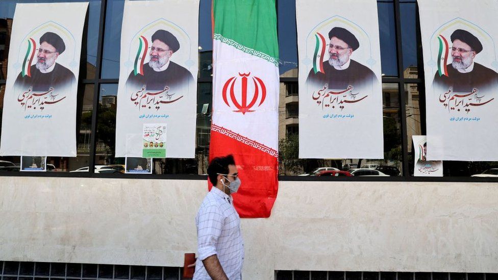 Man walking past posters of Iranian president-elect Ibrahim Raisi