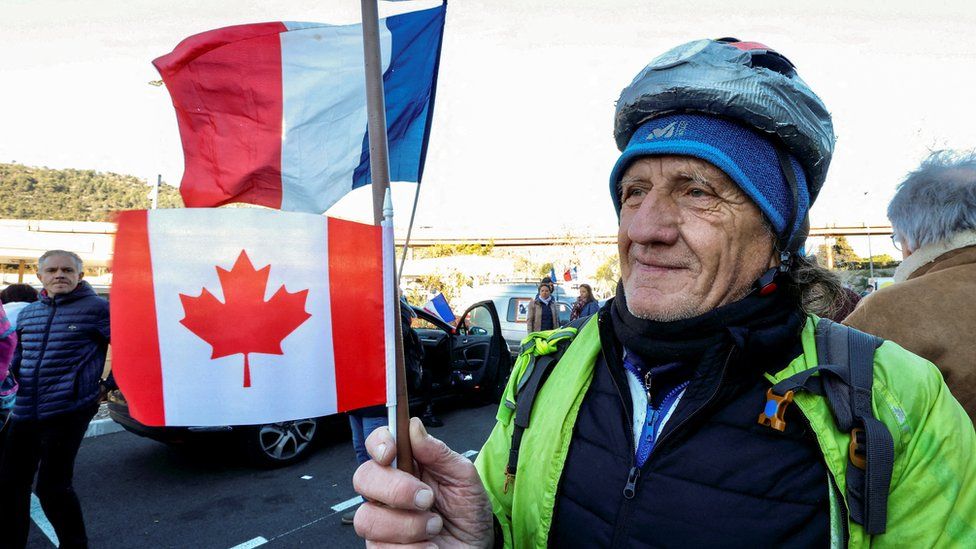 Мужчина держит трость с флагами Канады и Франции