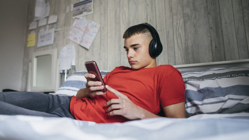 Adolescent looking a his phone while lying on his bed