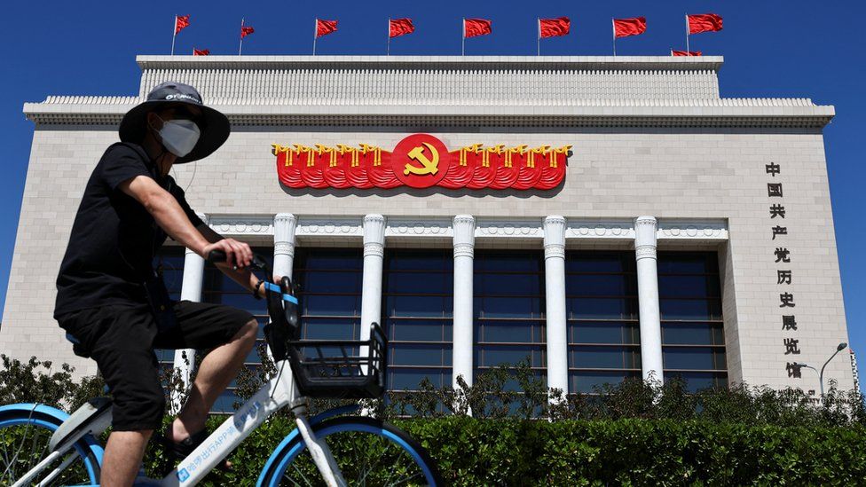 Person rides a bicycle of a bike sharing service past the Museum of the Communist Party of China in Beijing